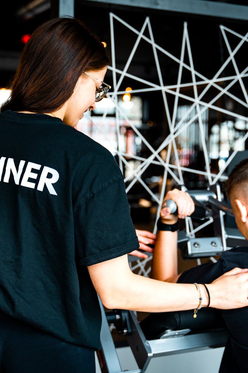 Trainerin betreut Mitglied persönlich an der Maschine im Fitnessstudio Bitburg GymOne 24/7