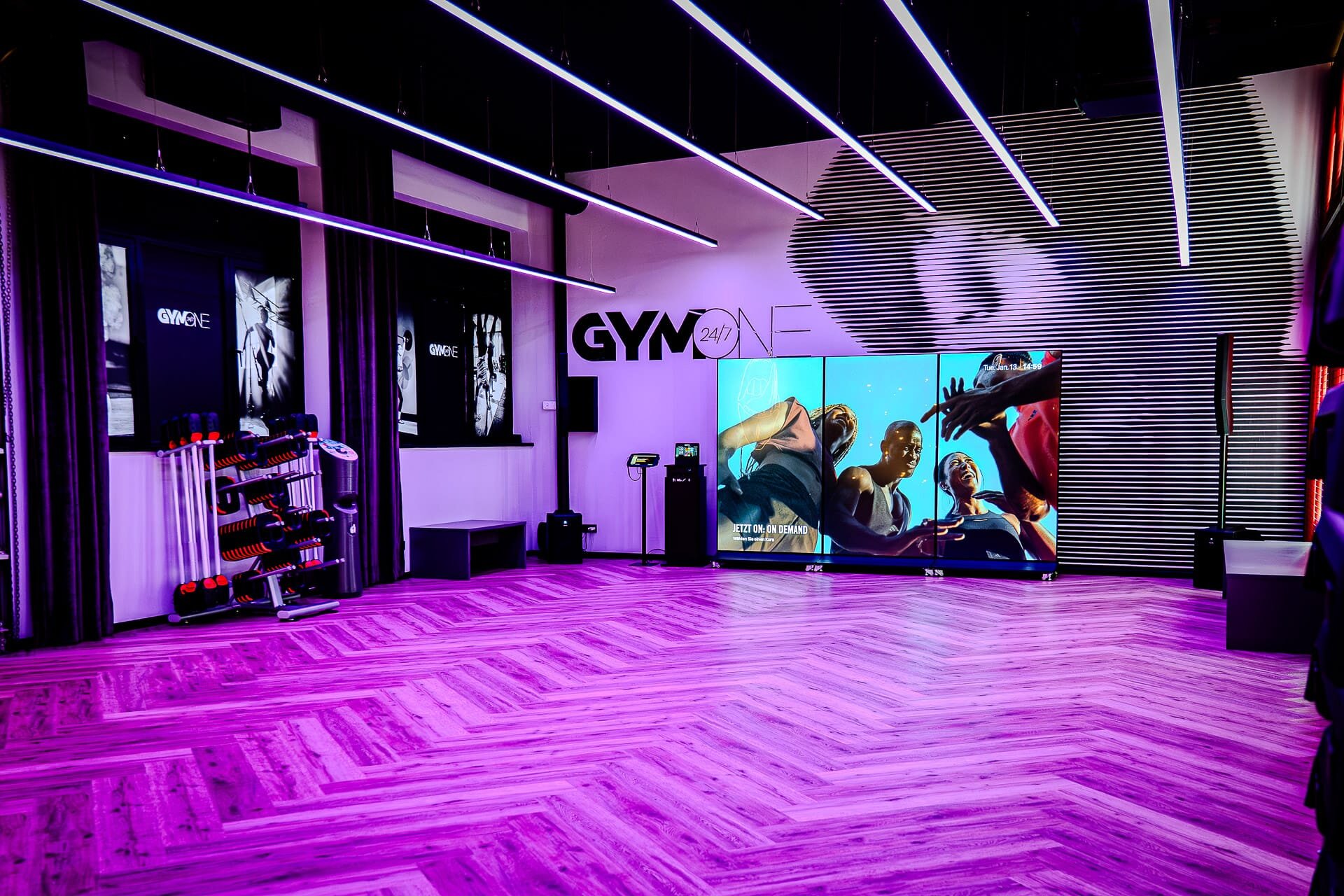 Les Mills Kursraum mit violetter LED-Beleuchtung und großem On-Demand Bildschirm im Fitnessstudio Bitburg GymOne 24/7